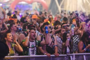 Energetic crowd at a music festival enjoying live performances with drinks.
